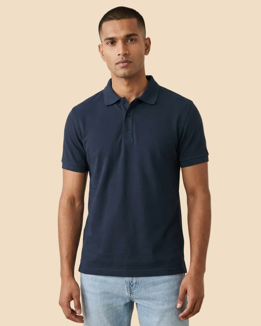 A man wearing a navy blue short-sleeve polo shirt and light blue jeans, standing against a plain beige studio background.