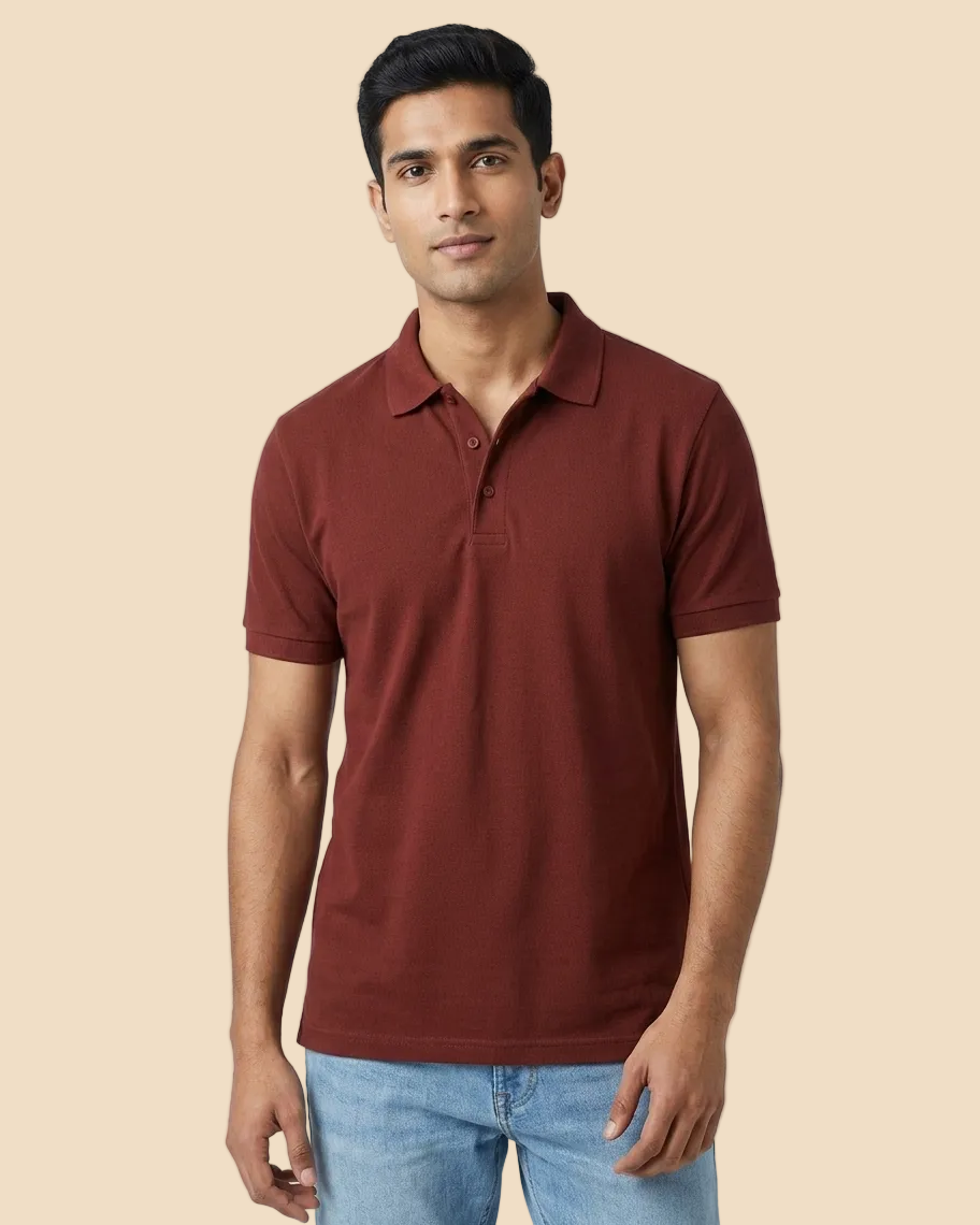 A man wearing a short-sleeve polo shirt in a deep rust red color, paired with light blue jeans, standing against a light gray studio background.