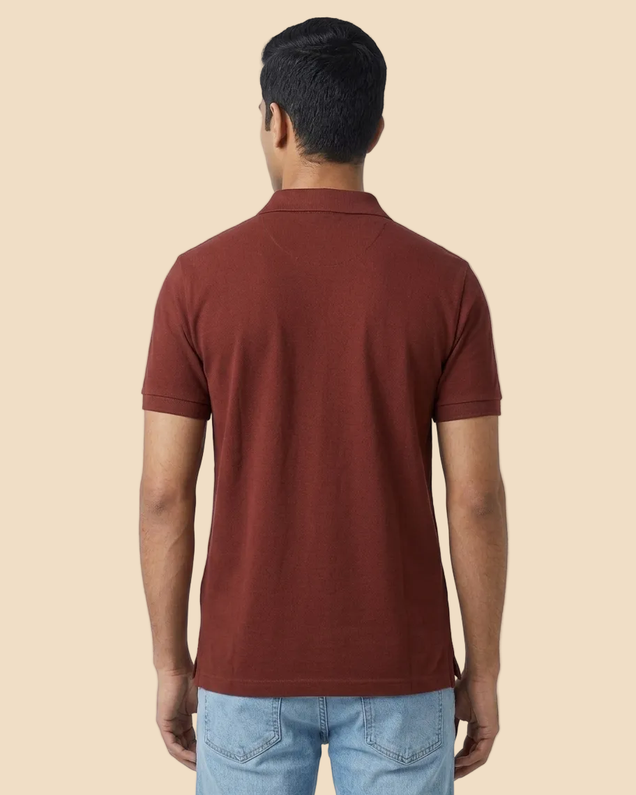 A man viewed from behind wearing a short-sleeve polo shirt in a muted reddish-brown color, paired with light blue jeans, against a plain peach background.