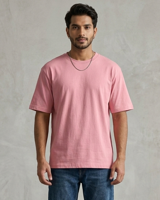 Man wearing a pink t-shirt and blue jeans standing against a plain wall.