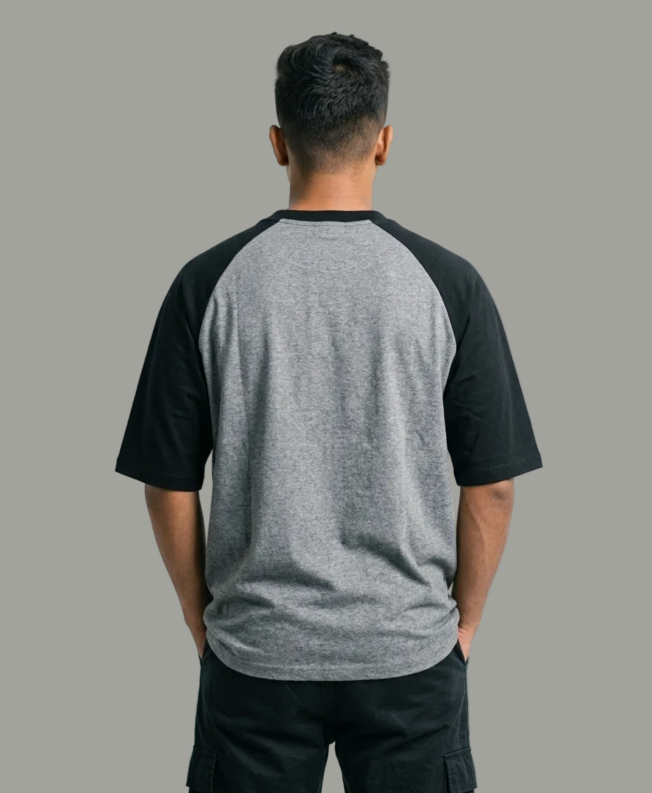 A man viewed from behind wearing a heather gray and black raglan t-shirt, paired with black cargo pants, against a plain white studio background.