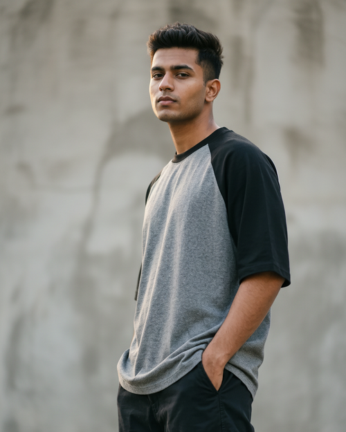 A man wearing a gray and black raglan t-shirt and dark cargo pants, standing against a textured concrete wall.