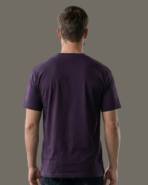 Man wearing a purple t-shirt and dark jeans standing in a modern room with large windows.