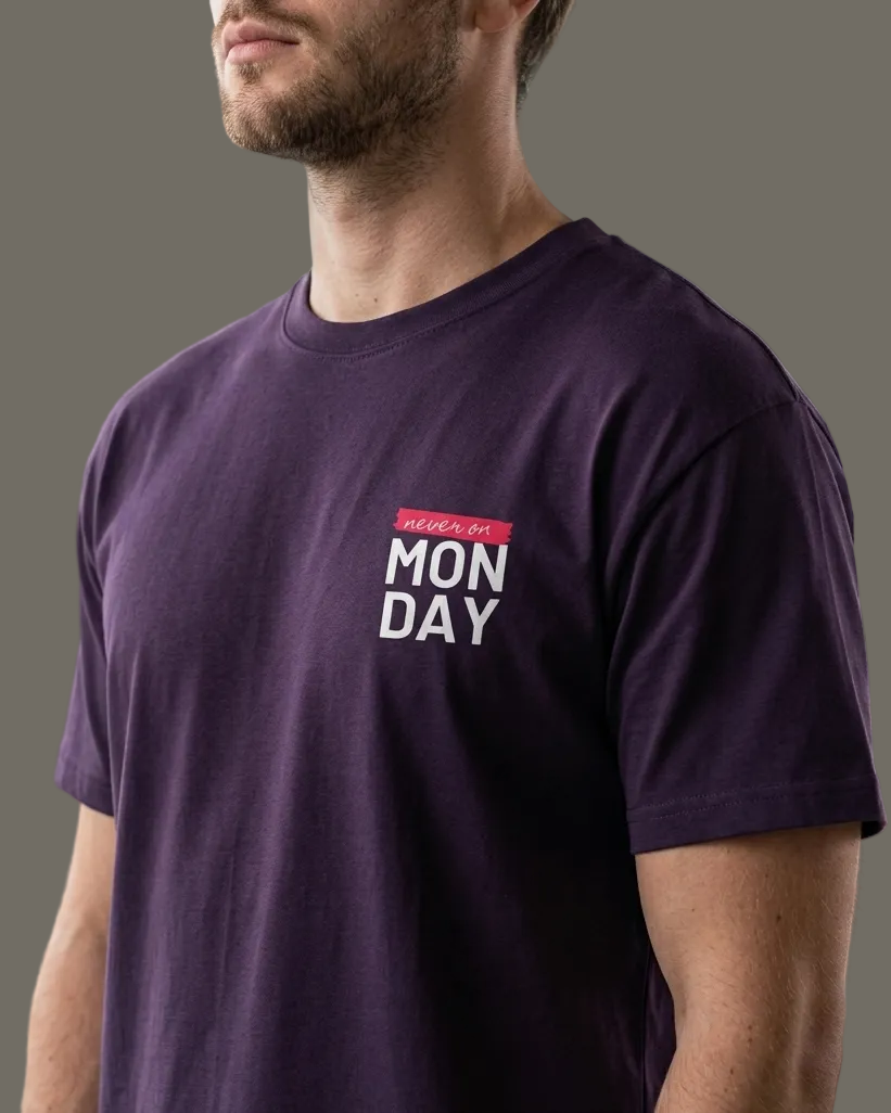 Man wearing a purple t-shirt with 'Monday' text in a room with large windows.