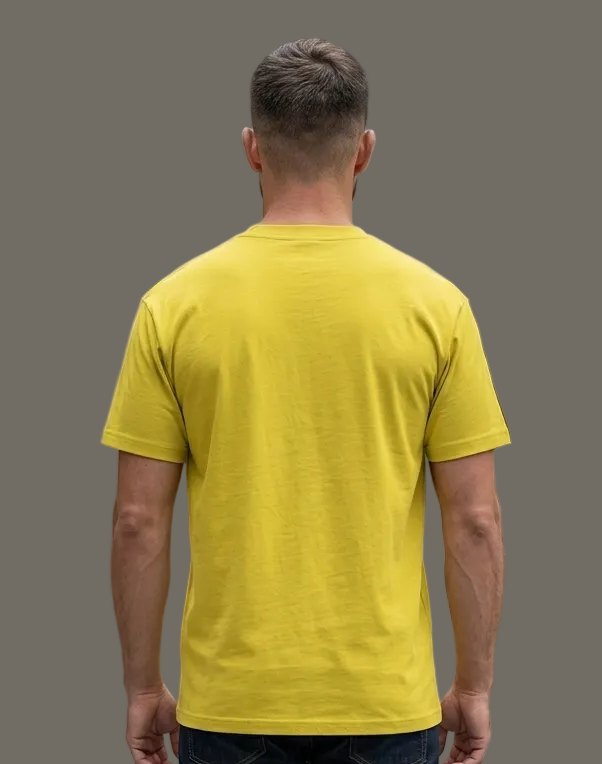 Man wearing a yellow t-shirt and dark jeans in a grey background