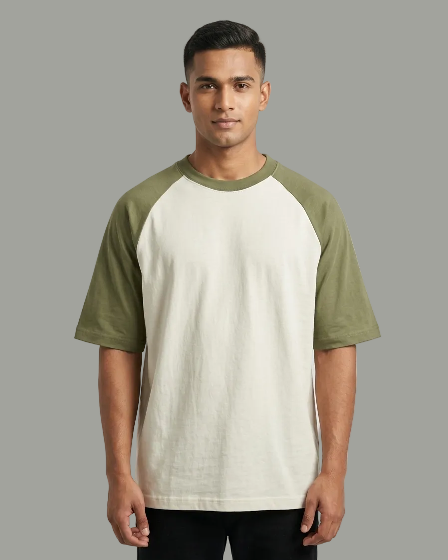 A man wearing a short-sleeve raglan t-shirt with an off-white body and olive green sleeves, standing against a light gray studio background.