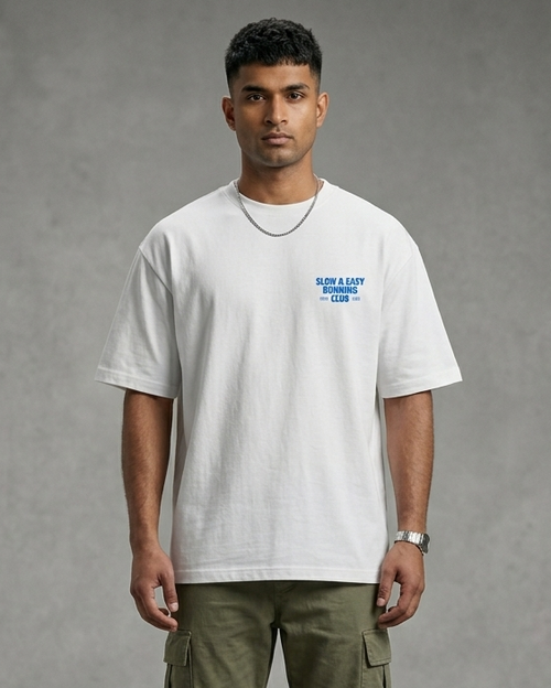 Man wearing a white t-shirt with a logo and green pants on a gray background