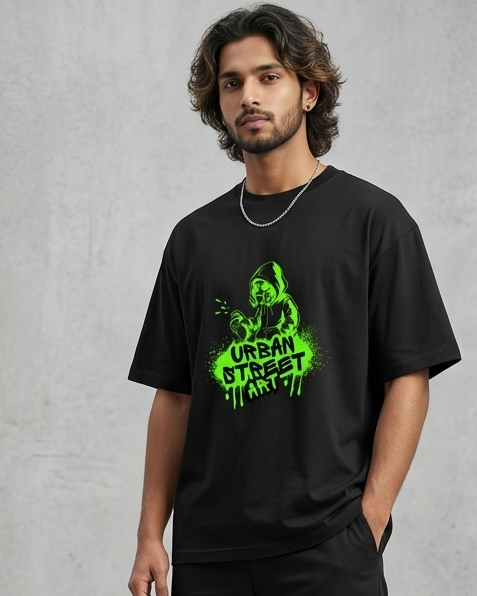 Person wearing a black t-shirt with green graphics and black cargo pants against a gray concrete wall.