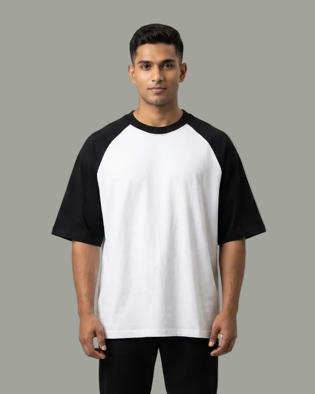 A man modeling a black and white raglan t-shirt with black pants, standing against a light gray studio background.